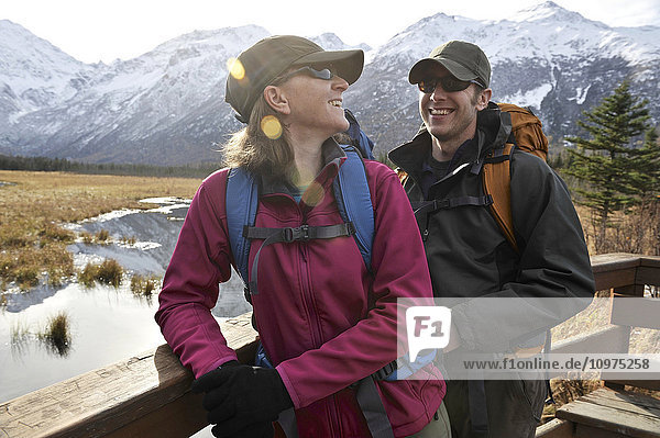 Ein Wanderpaar blickt von einer Aussichtsplattform auf dem Rodak Nature Trail im Chugach State Park in der Nähe des Eagle River Nature Center in Süd-Zentral-Alaska auf das Eagle River Valley und die Chugach Mountains