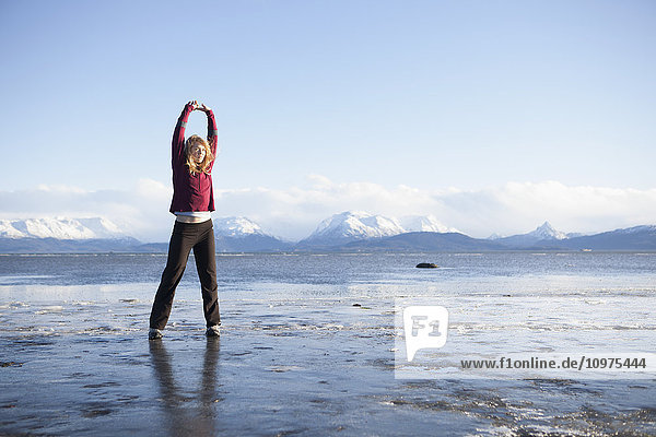 Frau  die sich vor einem Lauf am Strand von Homer auf einem vereisten Strand dehnt  Kenai-Halbinsel  Süd-Zentral-Alaska