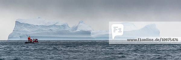Schlauchboot steuert auf blauen Eisberg am Horizont zu; Antarktis