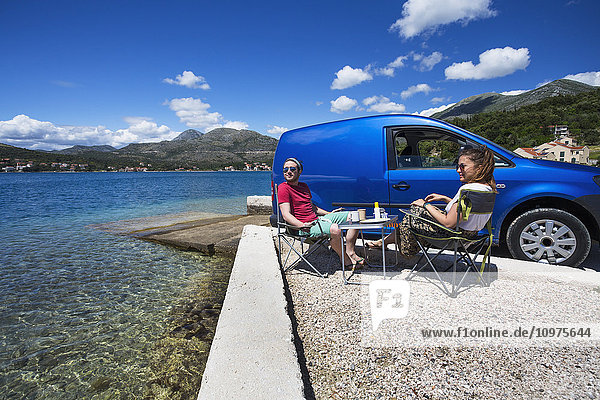 Ein Paar sitzt vor seinem Wohnmobil an einem Strand entlang der Küste; Slano  Kroatien'.