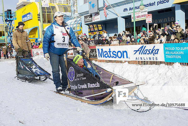 Jessie Royer und ihr Team verlassen die feierliche Startlinie mit einem Iditarider während des Iditarod 2016