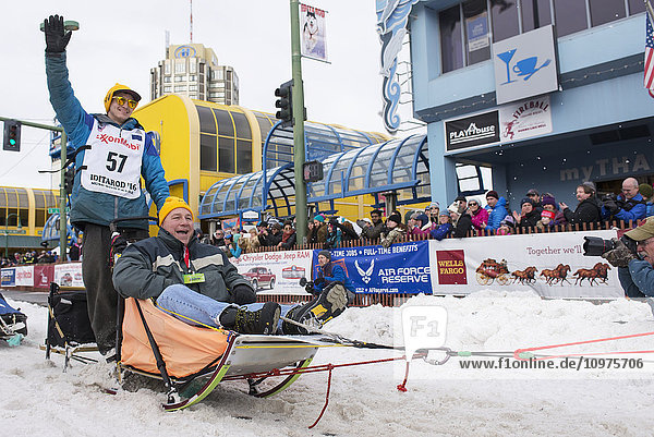 Robert Redington und sein Team verlassen die feierliche Startlinie mit einem Iditarider während des Iditarod 2016