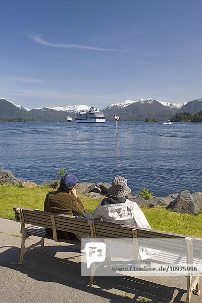 Tourists Relax On A Bench Along The Shore With A View Of A Celebrity And A Holland America Cruise Ship Anchored At Sitka  Alaska