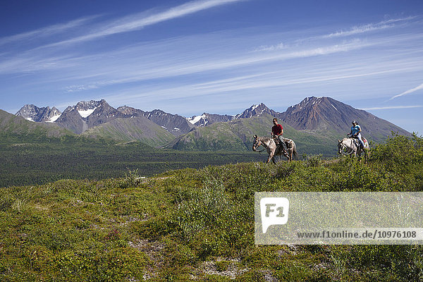 Visitors on horseback trail ride out of Rainy Pass Lodge with the Alaska Range background  Southcentral Alaska  Summer