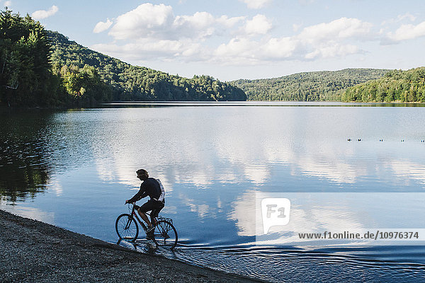 Radfahrer fährt durch flaches Wasser am Rande eines Sees; Waterbury  Vermont  Vereinigte Staaten von Amerika'.