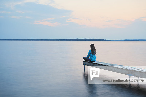 Mädchen sitzt am Ende des Stegs bei Sonnenaufgang am Balsam Lake; Ontario  Kanada'.