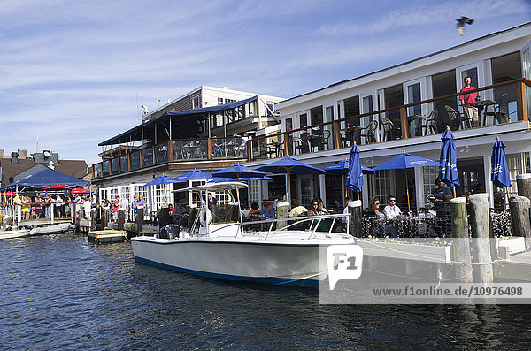'People sitting at bar and eating meal at Landings Restaurant at the deck tables  speed boat at dock  Bowen's Wharf; Newport  Rhode Island  United States of America'