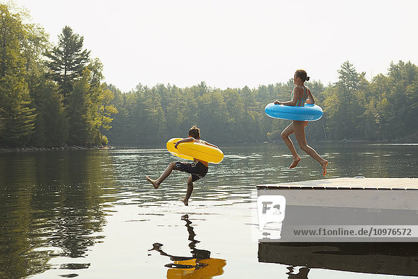 Kinder springen vom Ende eines Stegs mit aufblasbaren Ringen am Crystal Lake; Ontario  Kanada'.