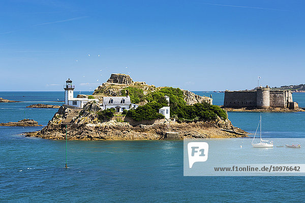 Weißer Leuchtturm auf einer Insel mit steinerner Burg und Türmchen ebenfalls auf einer Insel im Hintergrund mit blauem Wasser und Himmel; Carantec  Bretagne  Frankreich'.