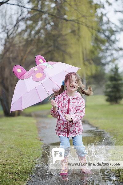 Junges Mädchen springt in eine Pfütze und hält einen Regenschirm; Toronto  Ontario  Kanada'.