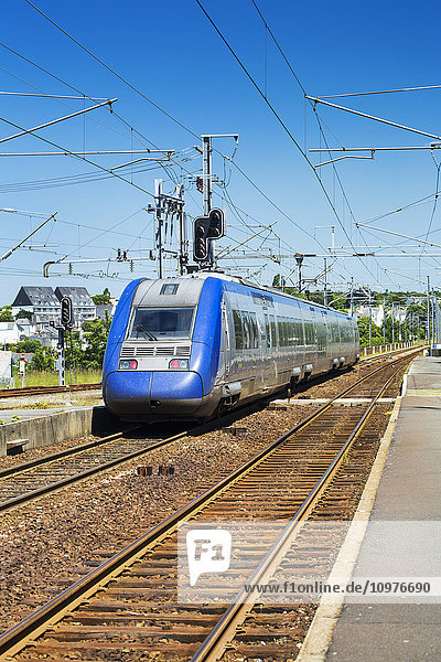 Stromlinienförmiger elektrischer Zug auf Gleisen an einem Bahnsteig mit blauem Himmel; Morlaix  Bretagne  Frankreich'.