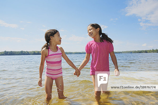 Zwei Schwestern halten sich an den Händen und spielen im Crystal Lake; Ontario  Kanada'.