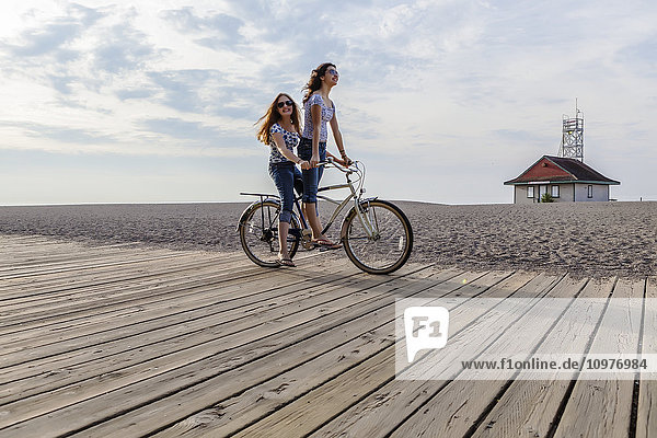 'Two girls riding double on a single bike on a beach boardwalk; Toronto  Ontario  Canada'