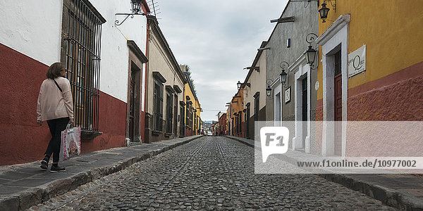 Fußgänger  der neben einer Straße mit Kopfsteinpflaster und bunten Gebäuden spazieren geht; San Miguel de Allende  Guanajuato  Mexiko'.