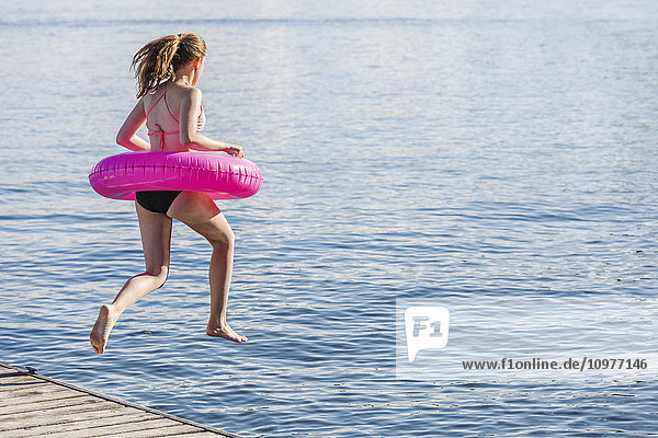 Mädchen springt von einem Steg am Balsam Lake und trägt einen aufblasbaren Ring; Ontario  Kanada'.
