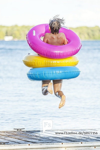 Junge springt mit bunten aufblasbaren Ringen vom Steg am Balsam Lake; Ontario  Kanada'.