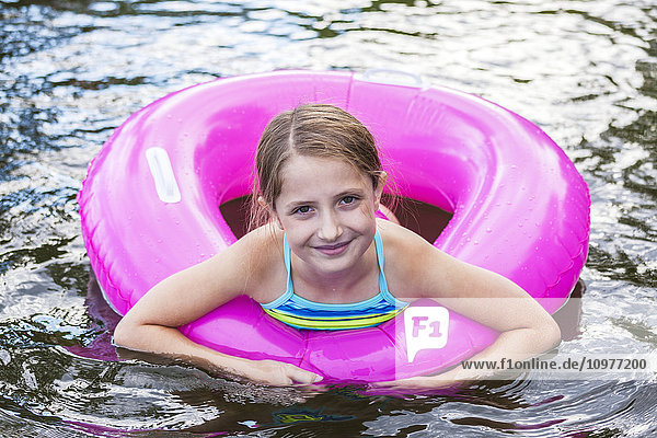 Porträt eines jungen Mädchens  das mit einem rosa aufblasbaren Schlauch in einem See schwimmt; Ontario  Kanada'.