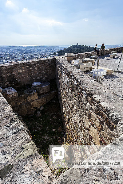 Ein Paar sitzt auf einer Steinmauer mit Blick auf die Stadt; Athen  Griechenland'.