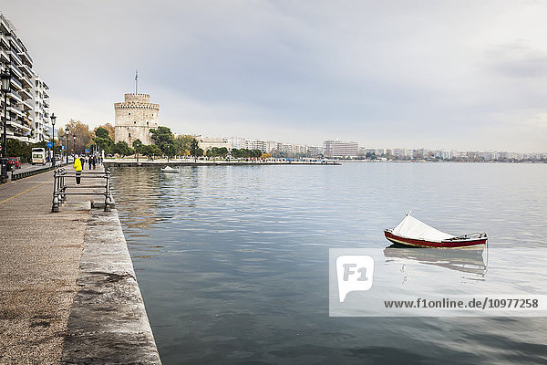 Ein einsames Boot  das im Wasser entlang der Uferpromenade vertäut ist  mit dem Weißen Turm in der Ferne; Thessaloniki  Griechenland
