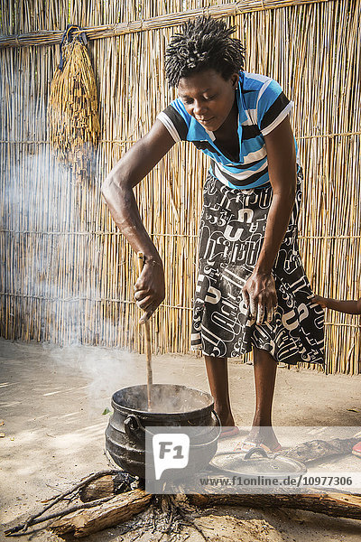 Afrikanische Frau aus dem Dorf Sexaxa rührt das Sorghum für das Familienessen; Maun  Botswana