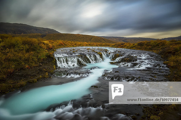 'Long exposure of water flowing over rock in a stream and dark clouds in the sky; Bruarfoss  Iceland'
