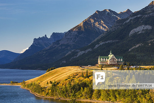 Prince of Wales Hotel auf einer Bergkuppe bei Sonnenaufgang mit Blick auf einen See mit Bergen im Hintergrund und blauem Himmel; Waterton  Alberta  Kanada'.