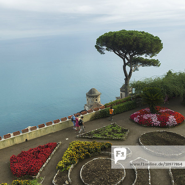 'Pedestrians along a walkway with colourful flowers in bloom and a view of the ocean; Ravello  Italy'