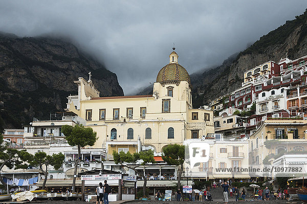 Ein Kirchengebäude und Häuser an einem Hang mit Fußgängern an der Amalfiküste; Positano  Kampanien  Italien'.