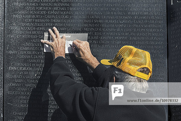 'Vietnam War veteran volunteer does a rubbing with a graphite pencil to get an imprint of name on memorial wall; Washington  District of Columbia  United States of America'