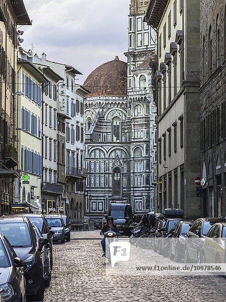 'A motorcyclist on a cobblestone street with Florence Cathedral in the background; Florence  Italy'