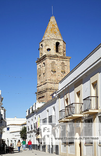 Fußgänger gehen eine Straße neben einem Wohnhaus und einem Turm entlang; Medina Sidonia de la Frontera  Andalusien  Spanien'.