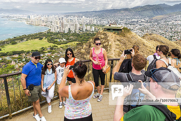 'Tourists taking family photos on Diamond Head with Honolulu Waikiki in the background; Honolulu  Oahu  Hawaii  United States of America'