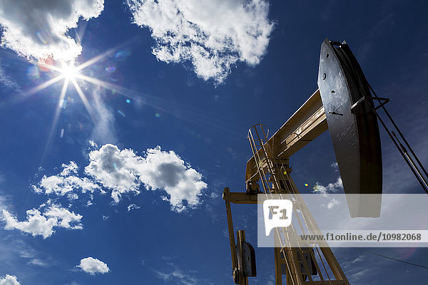 Niedriger Blickwinkel auf eine Pumpstation mit einer Sonneneruption am blauen Himmel und großen  bauschigen Wolken; Alberta  Kanada'.