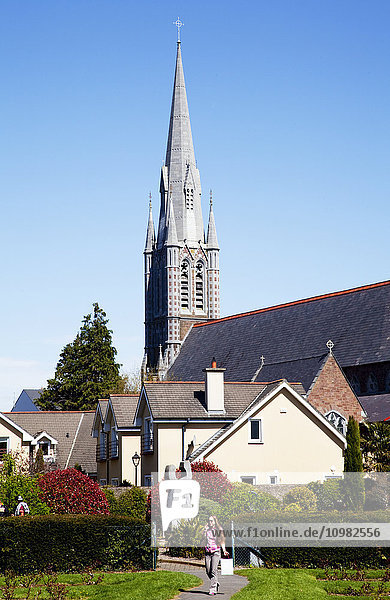Kirchengebäude mit hohem Kirchturm und Kreuz vor blauem Himmel; Tralee  County Kerry  Irland