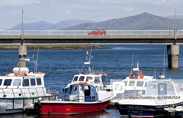 Im Hafen vertäute Boote und ein rotes Fahrzeug  das eine Brücke über das Wasser überquert; Portmagee  County Kerry  Irland