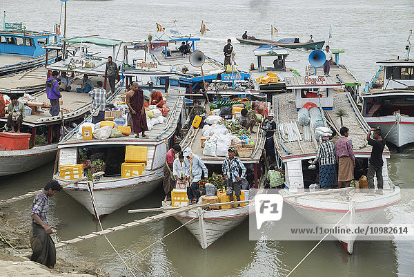 'Boats tied up on the Mandalay shore of the Irrawaddy River teaming with activity as they load goods and passengers; Mandalay  Myanmar'