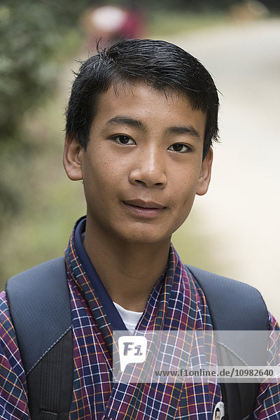 'Portrait of a boy with a checkered robe and carrying a backpack; Punakha  Bhutan'