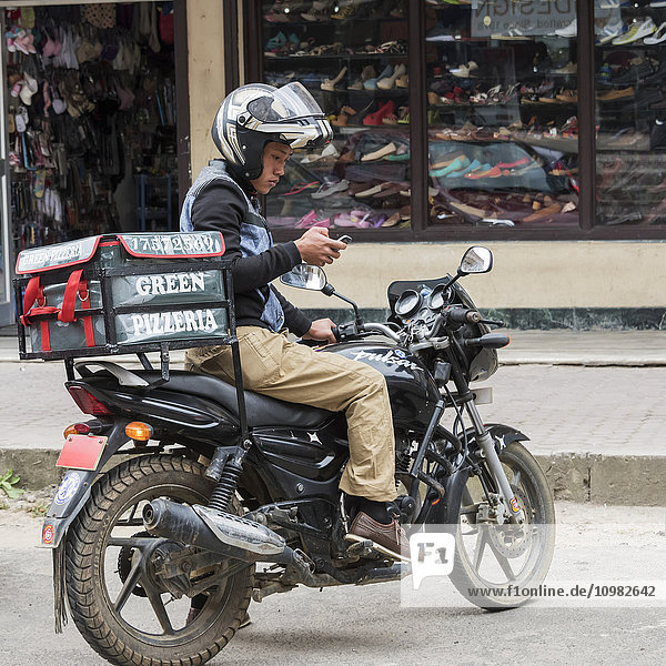 'Pizza delivery man on a motorcycle in the street using a smart phone; Thimphu  Bhutan'