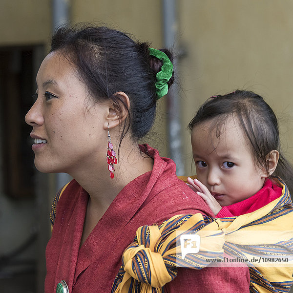 Eine Frau trägt ein kleines Mädchen auf dem Rücken; Paro  Bhutan'.