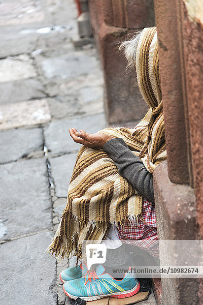 'An elderly woman sits on a step with hand open in her lap; San Miguel de Allende  Guanajuato  Mexico'
