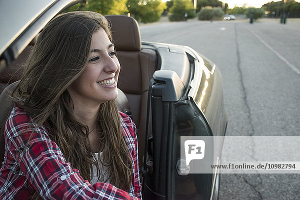 Lächelnde junge Frau im Cabrio sitzend