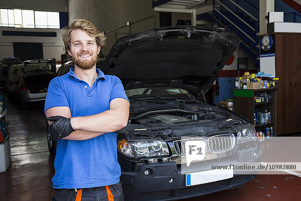 Confident mechanic standing in his car workshop with arms crossed
