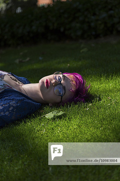 Portrait of young woman with dyed hair lying on a meadow