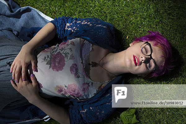 Portrait of young woman with dyed hair and eyes closed lying on a meadow