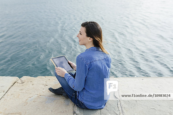 Junge Frau sitzend auf dem Dock mit digitalem Tablett