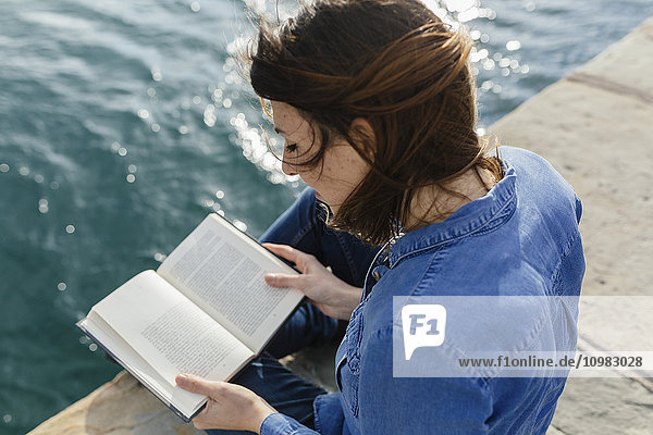 Junge Frau sitzt auf dem Dock und liest ein Buch.
