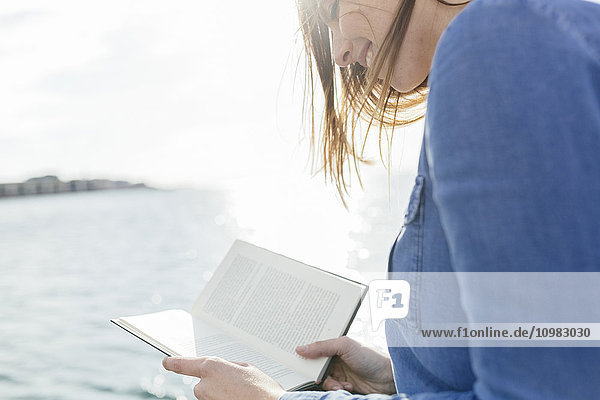 Junge Frau beim Lesen eines Buches am Wasser