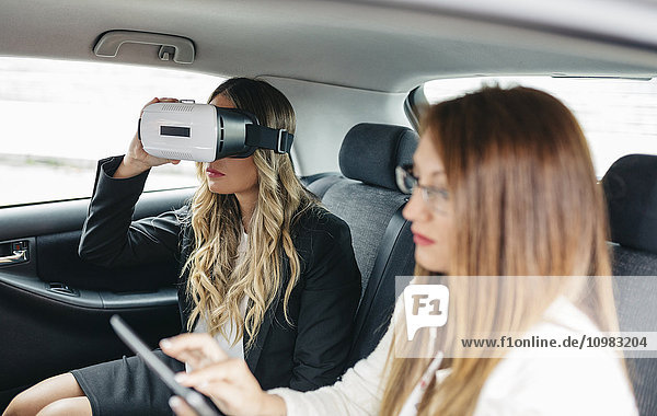 Zwei Geschäftsfrauen mit VR-Brille und digitalem Tablett im Auto