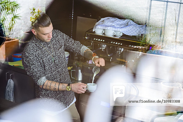 Junger Mann bereitet Kaffee mit Milch in einem Café zu.