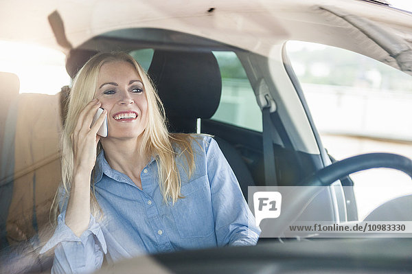 Lächelnde Frau im Auto am Handy